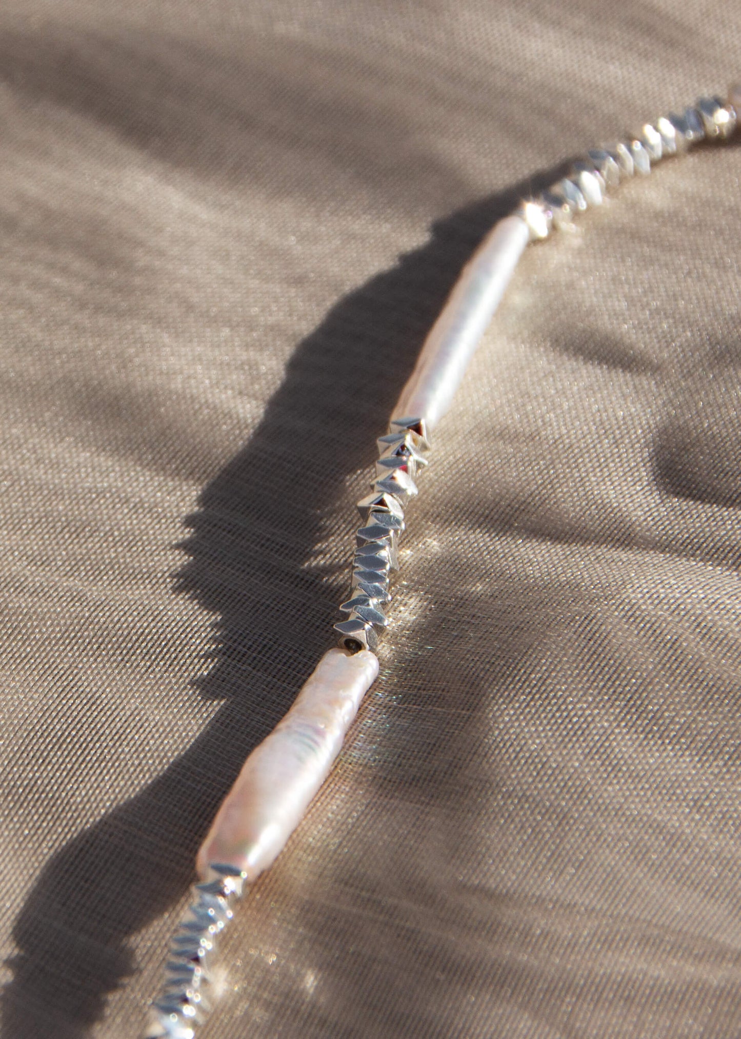 En fin silverkedja med stavformade pärlor och små silverpärlor i olika former för en naturinspirerad och texturerad design.