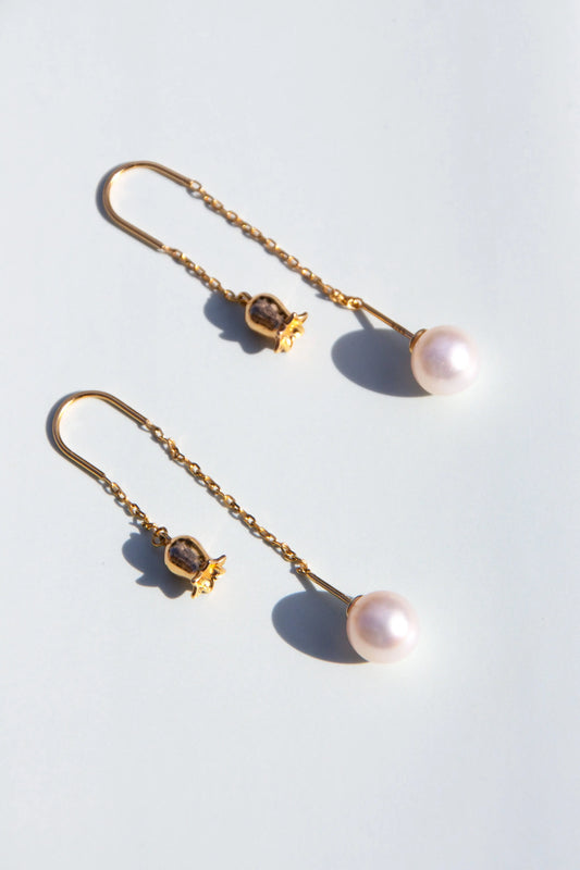 Pair of pearl earrings with gold chains on a light blue background