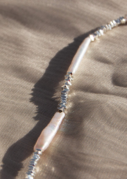En fin silverkedja med stavformade pärlor och små silverpärlor i olika former för en naturinspirerad och texturerad design.