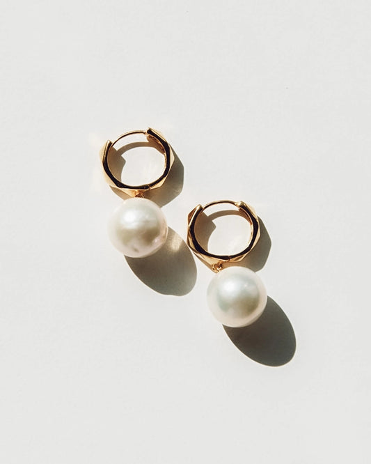 Gold hoop earrings with pearl drops on a light gray background