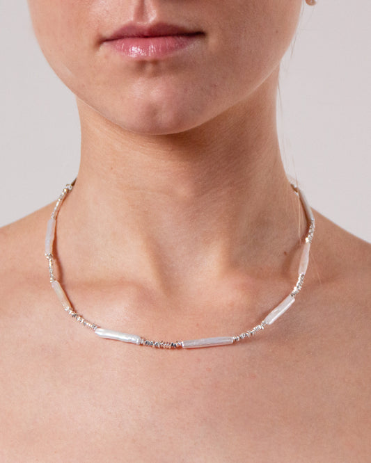 En fin silverkedja med stavformade pärlor och små silverpärlor i olika former för en naturinspirerad och texturerad design.