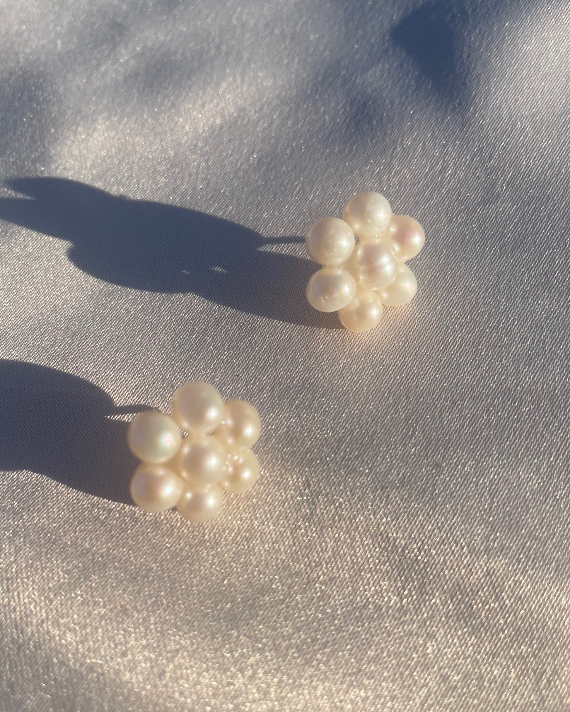 Fina pärlörhängen i prästkrageform som glittrar i solen, med glänsande pärlor som formar blomman.