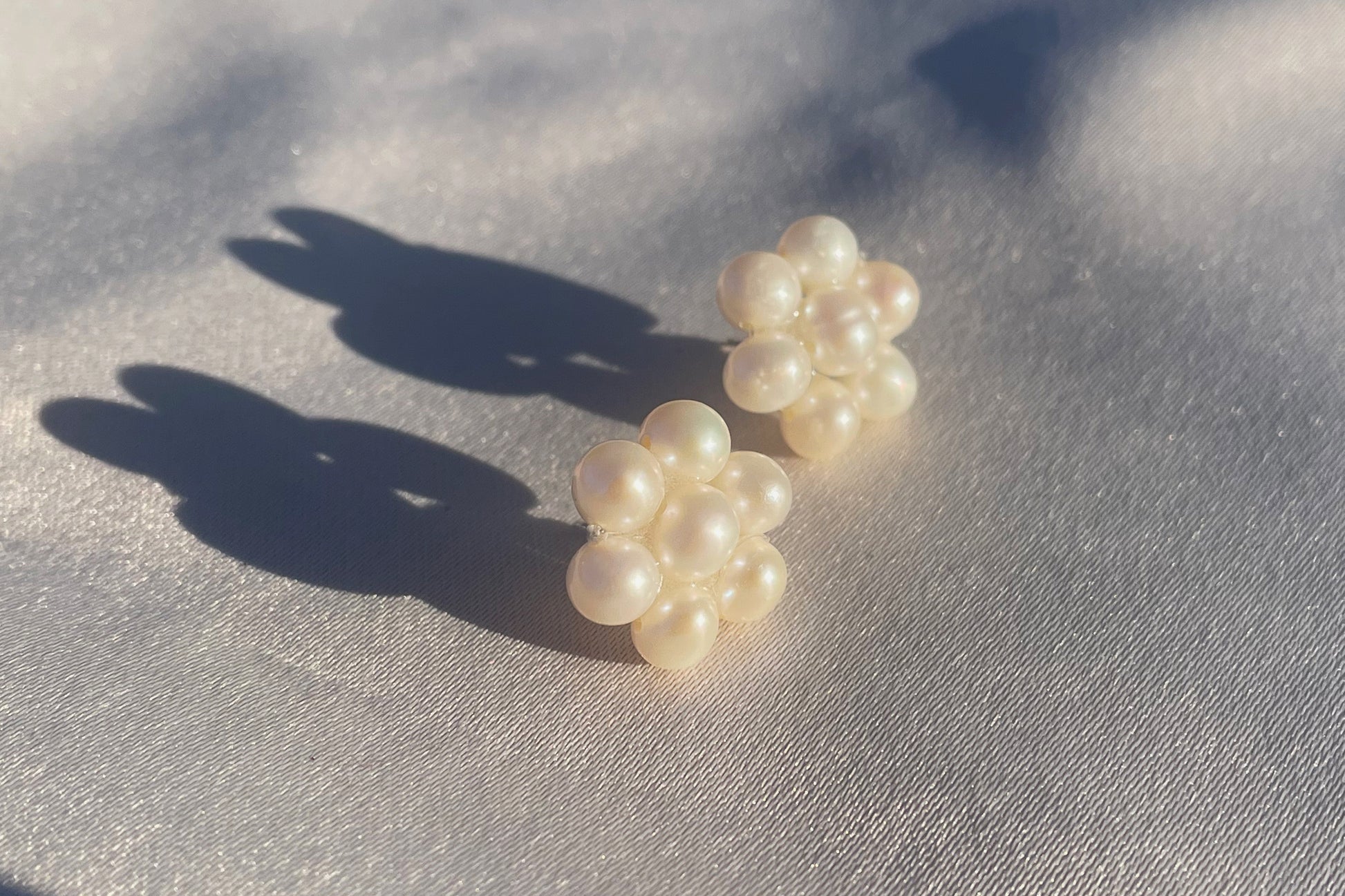 Fina pärlörhängen i prästkrageform som glittrar i solen, med glänsande pärlor som formar blomman.