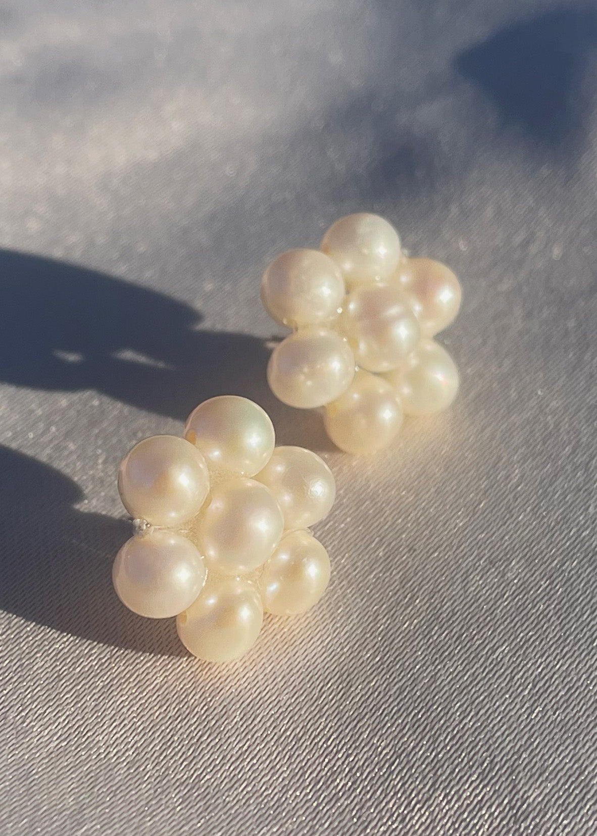 Fina pärlörhängen i prästkrageform som glittrar i solen, med glänsande pärlor som formar blomman.