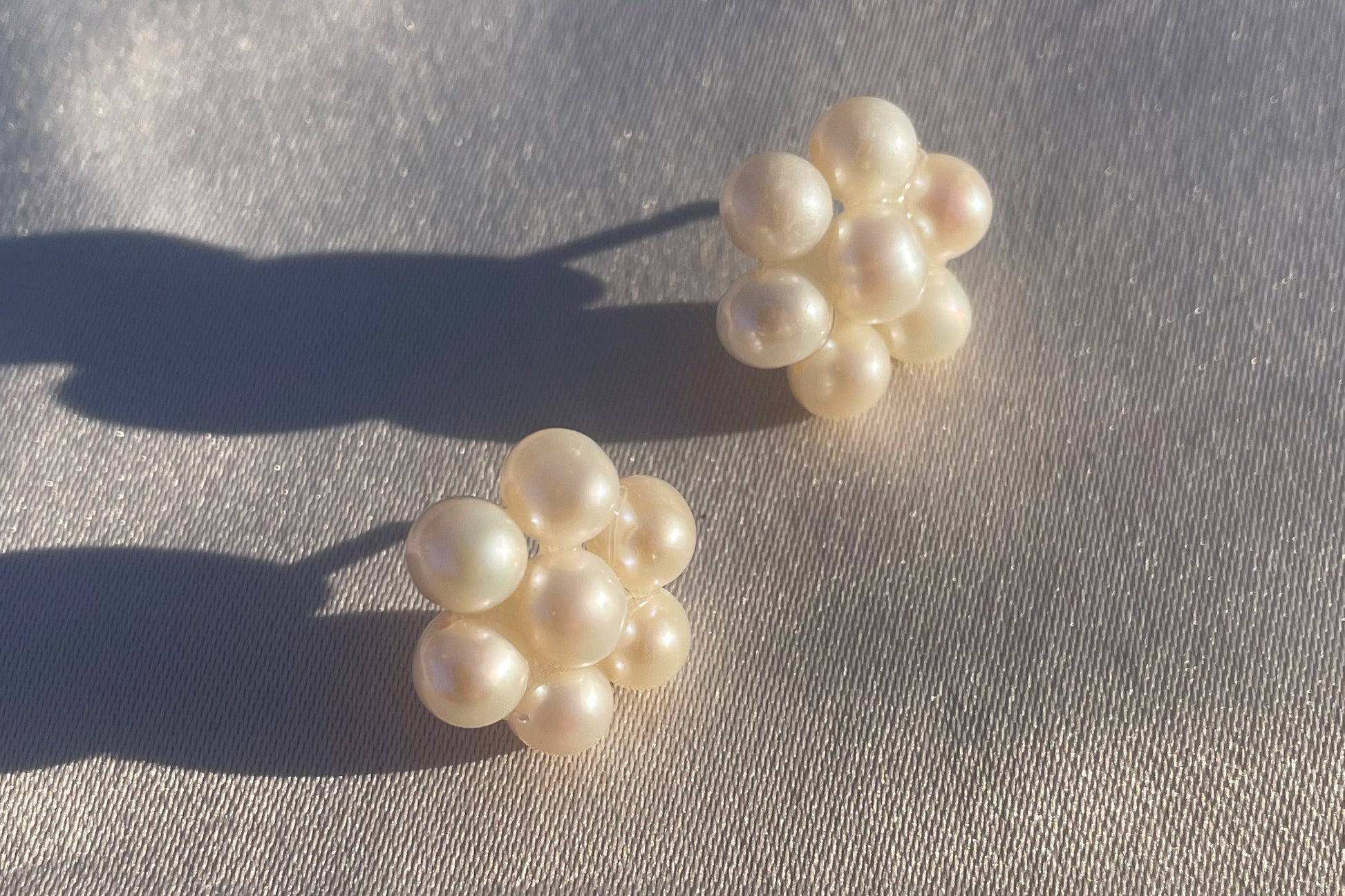 Fina pärlörhängen i prästkrageform som glittrar i solen, med glänsande pärlor som formar blomman.