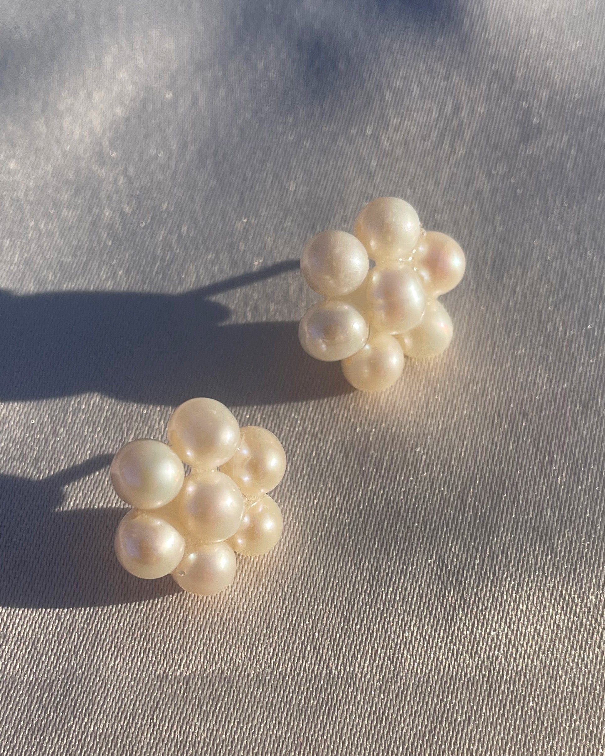 Fina pärlörhängen i prästkrageform som glittrar i solen, med glänsande pärlor som formar blomman.
