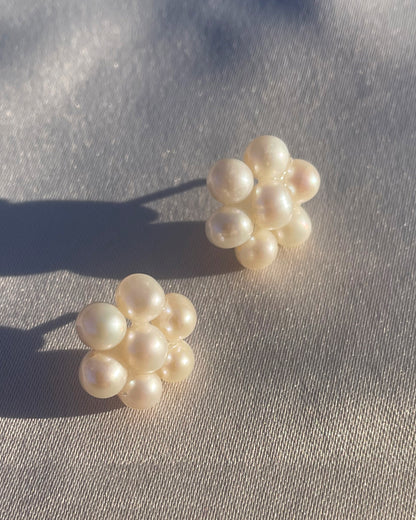 Fina pärlörhängen i prästkrageform som glittrar i solen, med glänsande pärlor som formar blomman.