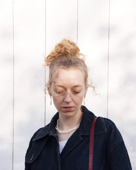 Person with blonde hair styled in a bun, wearing a pearl necklace and pearl earrings